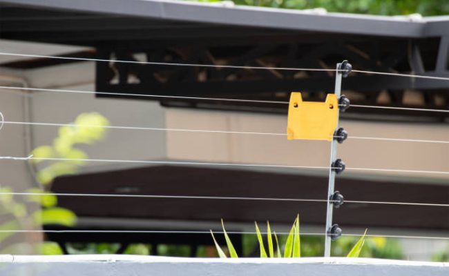 high voltage security fence on house wall with blank yellow plastic sign.